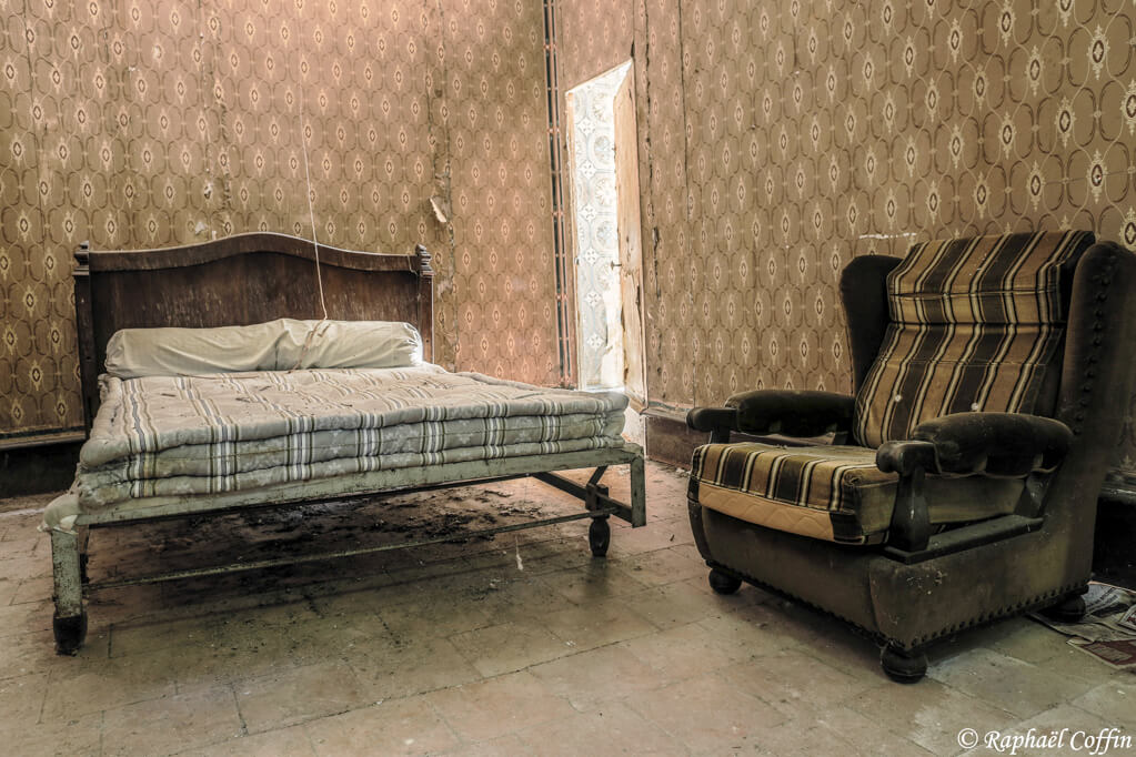 Vieux lit et fauteuil dans une villa abandonnée